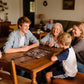 Multi-generational family playing backgammon on a roll-up 3-in-1 travel game set at a wooden dining table, ideal for family bonding and indoor entertainment.