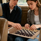 Couple playing chess on a beige roll-up travel game set in a car, perfect for road trip entertainment.