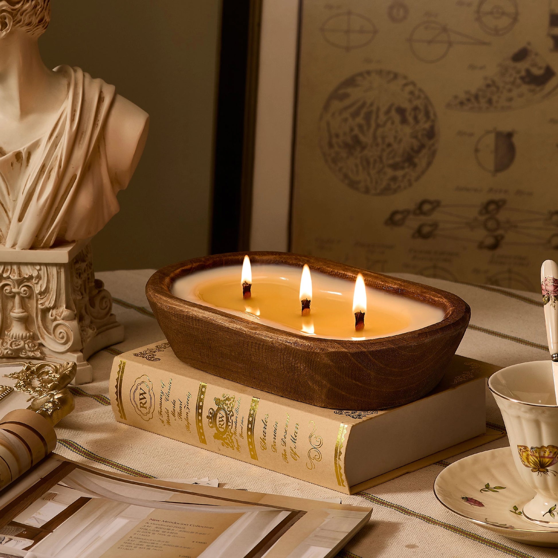 Lit three-wick candle in dark wood dough bowl, styled on vintage books for elegant home decor.